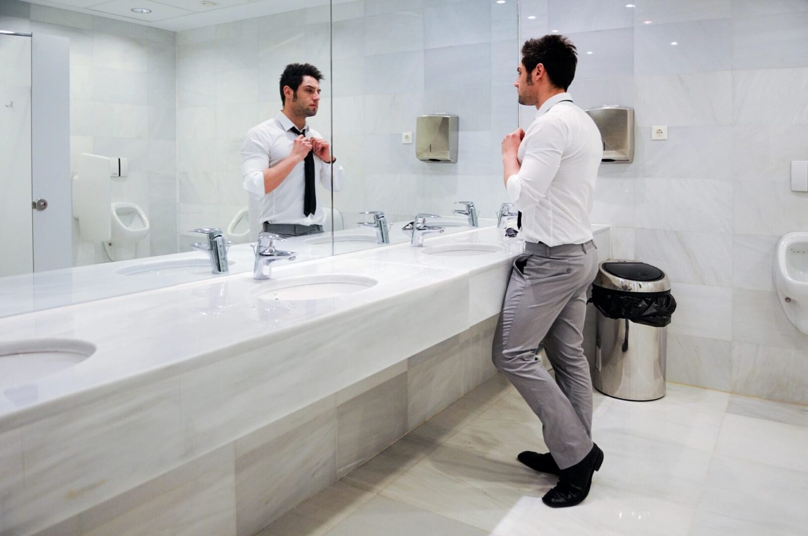 A man in white shirt and gray pants standing next to sink.