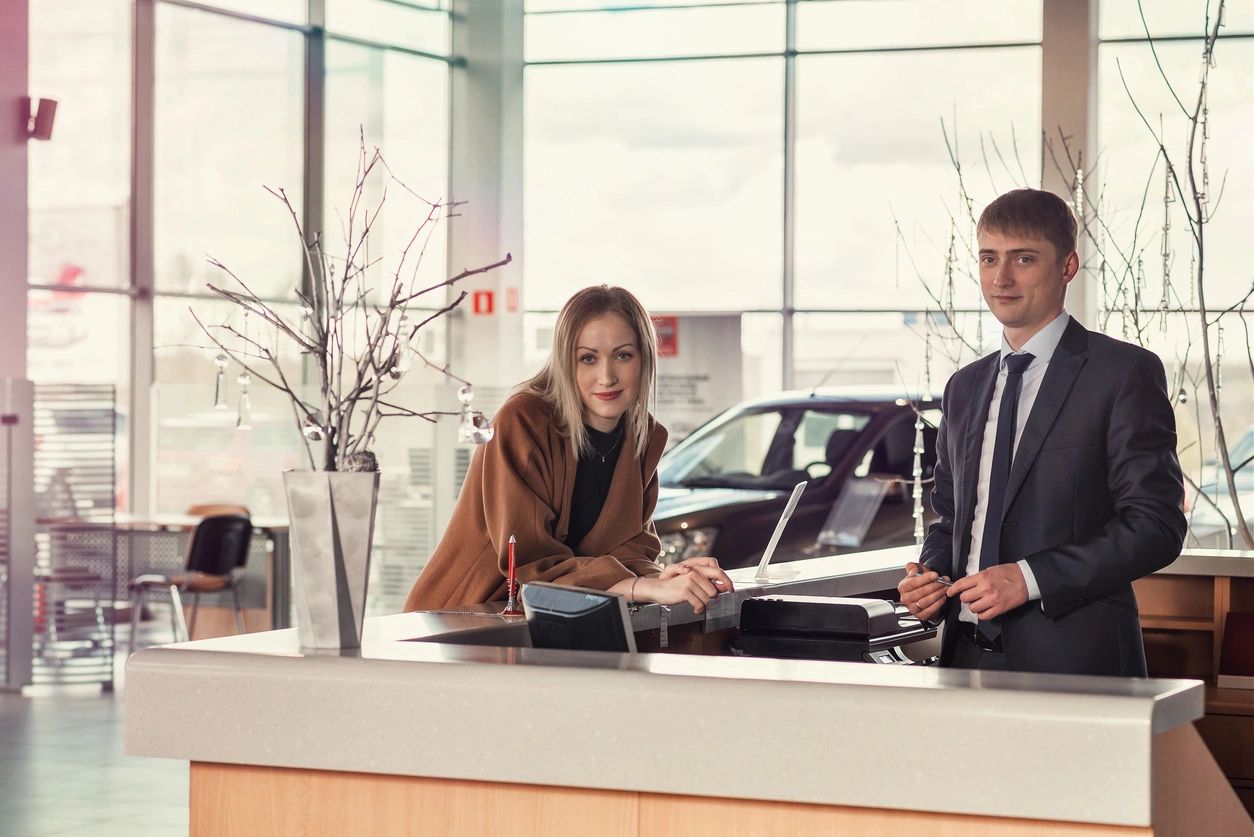 A man and woman in business attire standing at the counter of a car dealership.